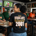 The best team in college football history
2001 National Champions
From The Orange Bowl Kid

 person is wearing a black t-shirt. The shirt displays a vertical column of well-known last names—Torretta, Searcy, Armstead, Barrow, Smith, Williams, and Huerta—in white, bold, block lettering with orange accents. A small orange emblem is seen on the right sleeve.